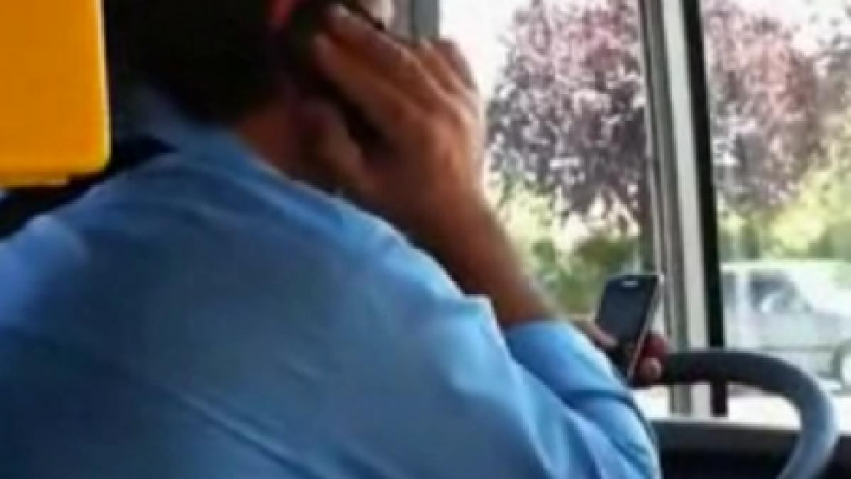 Un şofer de autobuz conduce vorbind la un telefon şi configurând e-mailul pe un altul 