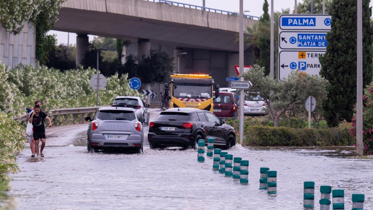 masini inainteaza prin apa si doi oameni merg pe jos pe o autostarad inundata in mallorca