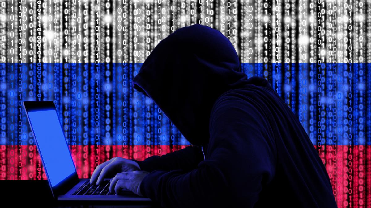 Ilustratie hacker tasteaza pe laptop cu steagul rusiei format din cod binar pe fundal.