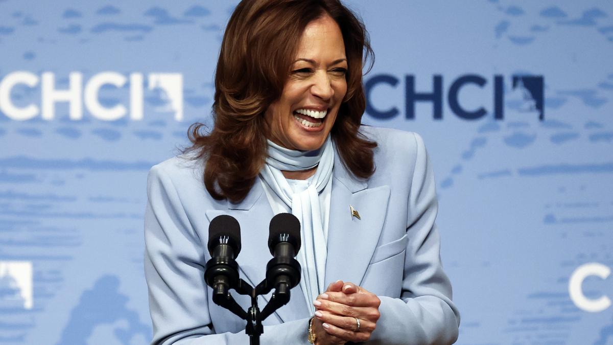 Kamala Harris intr-un sacou bleu, in fata unor microfoane, rade