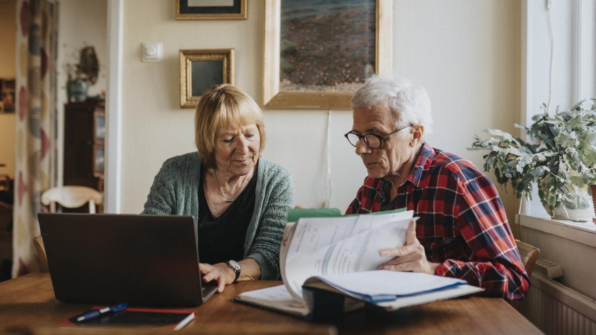 cuplu de pensionari verificand registre si laptop