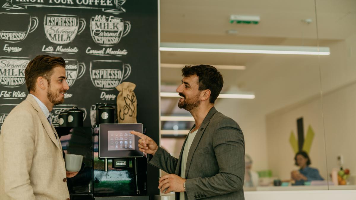 Doi barbati care stau de vorba ?n fata automatului de cafea