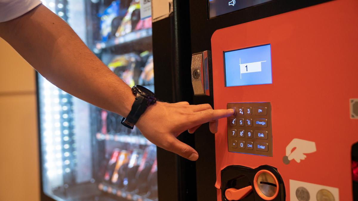 o persoana alege un produs de la un automat de gustari