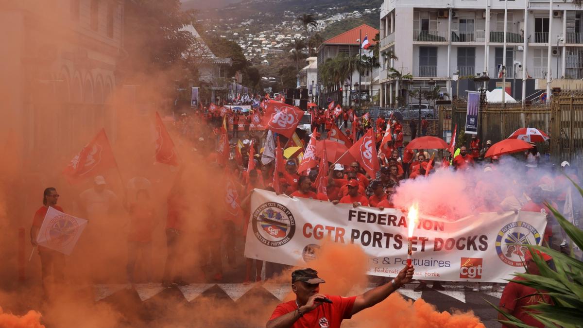 Oameni cu fumigene si banere in fum portocaliu la un protest in Martinica.