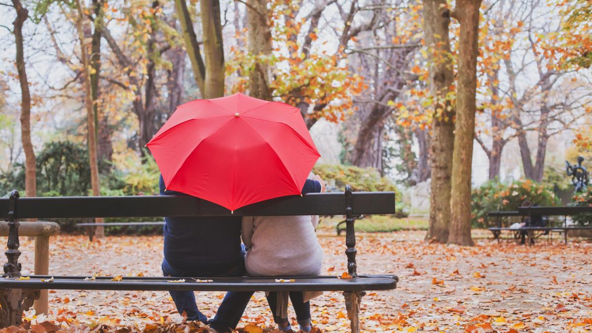 cuplu cu o umbrela pe banca in parc