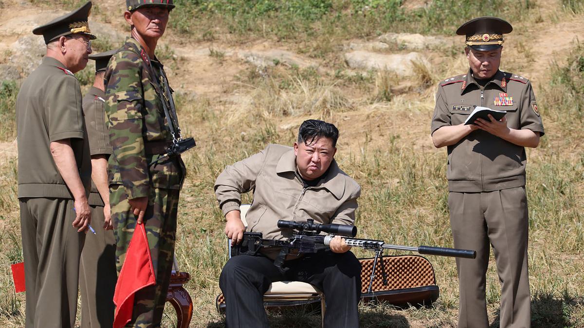 Kim Jong Un ține în mână o pușcă de asalt cu amortizor, înconjurat de soldați nord-coreeni.