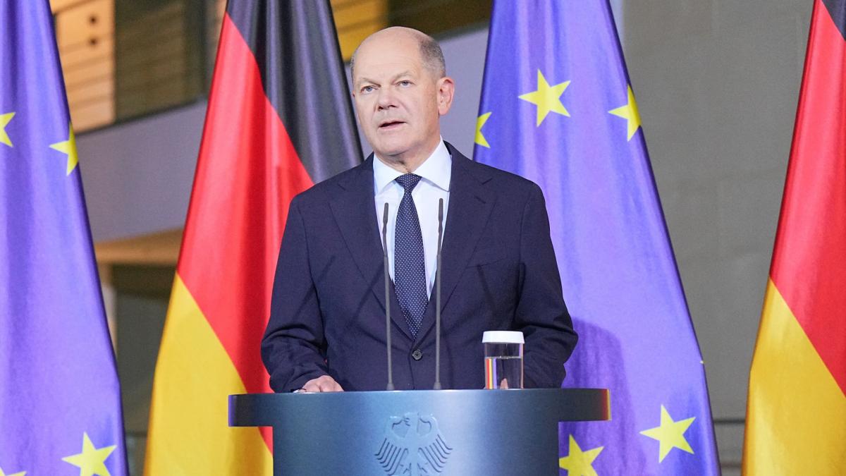 Scholz vorbește de la un podium cu steagurile UE și Germaniei în spate.