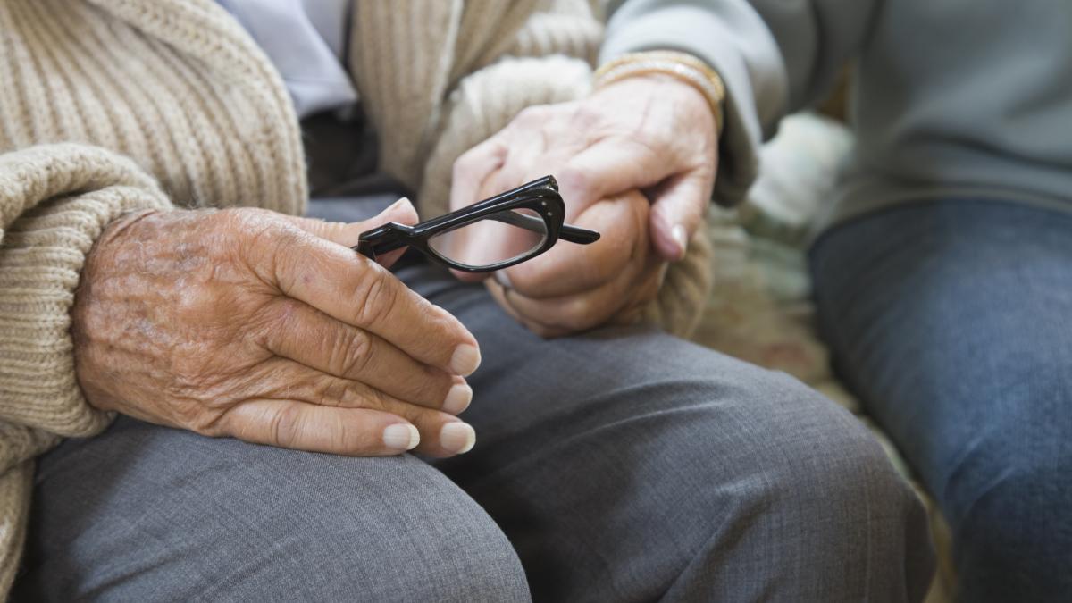 O femeie tine de mana un batran care are o pereche de ochelari in maini