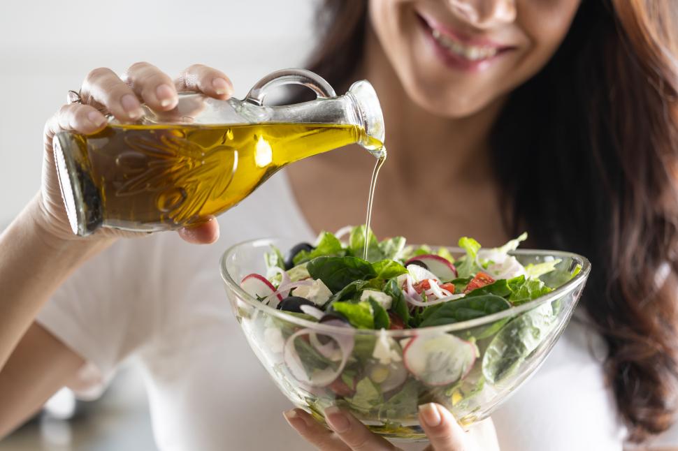 O femeie pune ulei de masline in salata