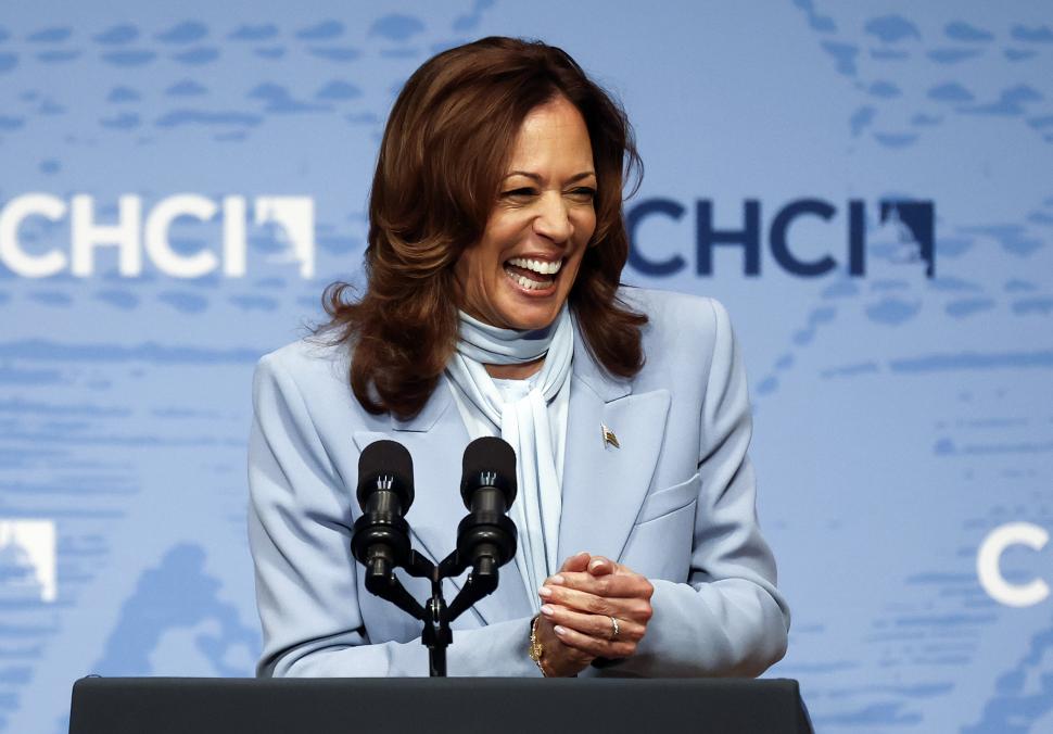 Kamala Harris intr-un sacou bleu, in fata unor microfoane, rade