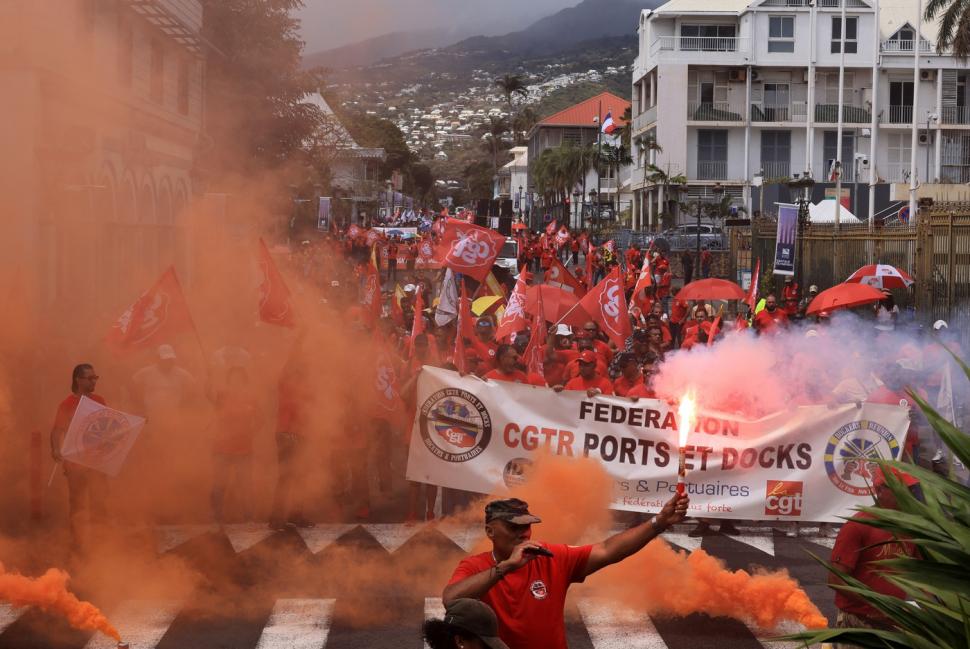 Oameni cu fumigene si banere in fum portocaliu la un protest in Martinica.